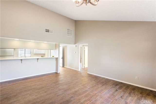 unfurnished living room featuring dark hardwood / wood-style floors, high vaulted ceiling, and a notable chandelier