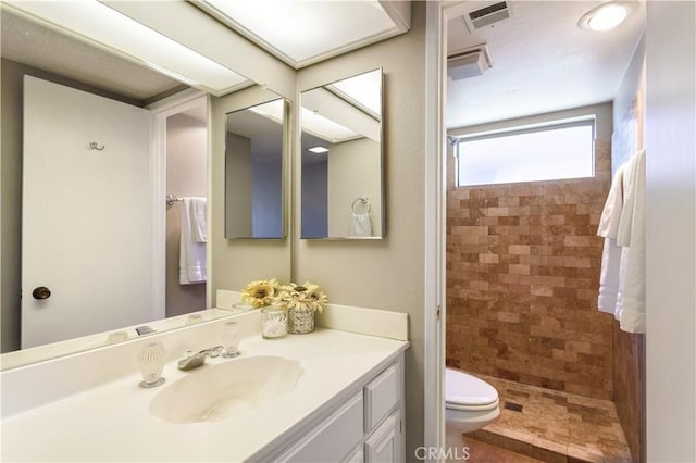 bathroom featuring a tile shower, vanity, and toilet