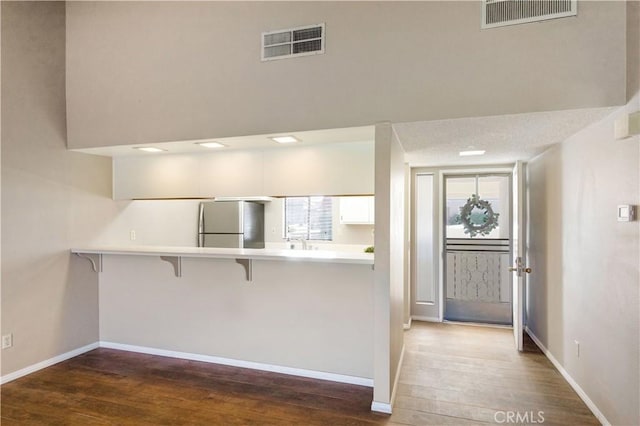 kitchen with stainless steel refrigerator, a breakfast bar, white cabinets, and dark hardwood / wood-style floors