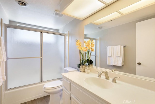 full bathroom featuring wood-type flooring, vanity, bath / shower combo with glass door, and toilet