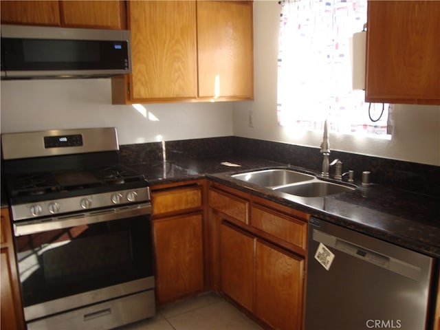 kitchen featuring stainless steel appliances, sink, dark stone counters, and light tile patterned floors