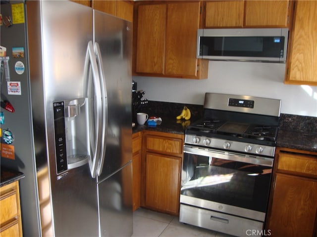 kitchen with stainless steel appliances, light tile patterned floors, and dark stone counters