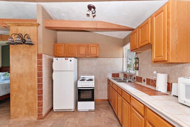 kitchen with lofted ceiling, tile countertops, sink, tile walls, and white appliances