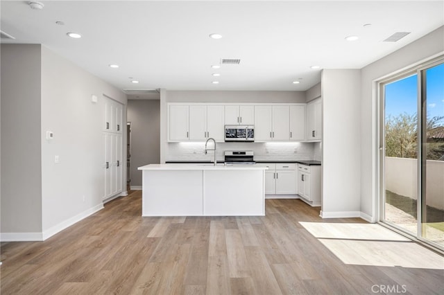 kitchen with tasteful backsplash, appliances with stainless steel finishes, white cabinetry, light hardwood / wood-style floors, and a center island with sink