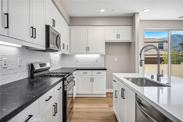 kitchen with sink, light wood-type flooring, white cabinetry, stainless steel appliances, and decorative backsplash