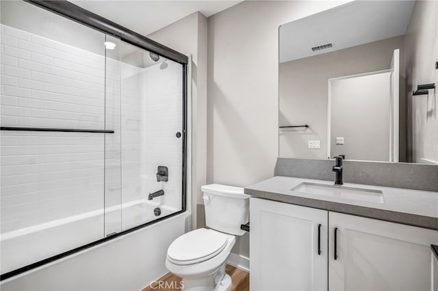 full bathroom with vanity, bath / shower combo with glass door, hardwood / wood-style flooring, and toilet