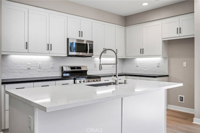 kitchen with appliances with stainless steel finishes, white cabinets, and a kitchen island with sink