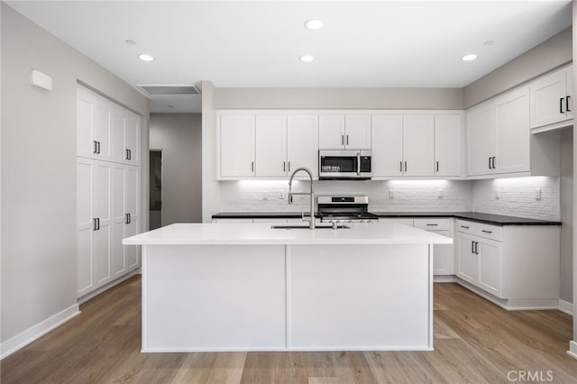 kitchen with stainless steel appliances, tasteful backsplash, light wood-type flooring, and white cabinets