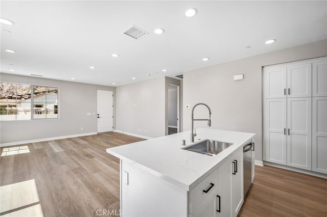 kitchen featuring a center island with sink, sink, light stone countertops, and light hardwood / wood-style floors