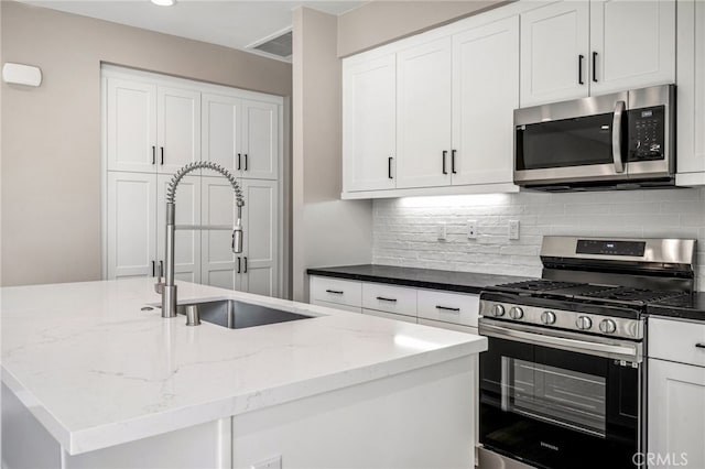 kitchen featuring backsplash, appliances with stainless steel finishes, an island with sink, white cabinetry, and light stone countertops