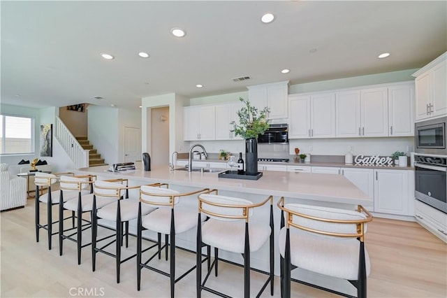 kitchen featuring sink, stainless steel appliances, a spacious island, white cabinets, and light wood-type flooring