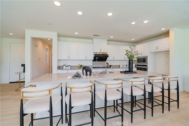 kitchen with a spacious island, a kitchen bar, sink, white cabinetry, and appliances with stainless steel finishes