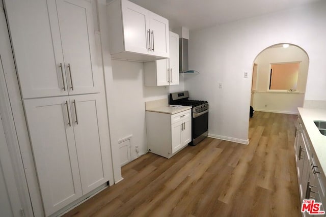 kitchen featuring stainless steel gas range, wall chimney range hood, white cabinets, and light hardwood / wood-style flooring