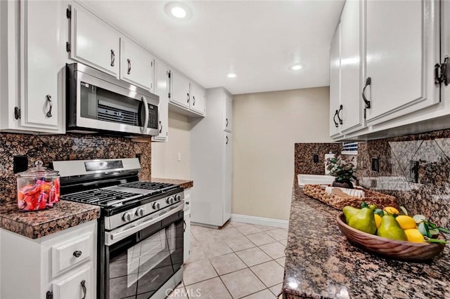 kitchen with dark stone countertops, appliances with stainless steel finishes, light tile patterned flooring, white cabinetry, and backsplash