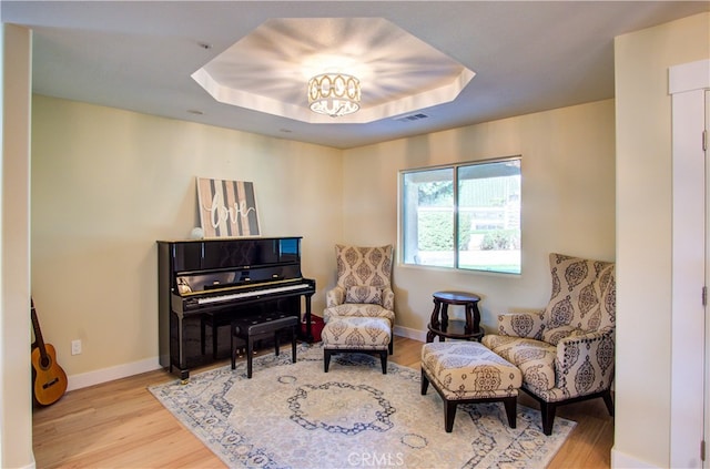 living area featuring an inviting chandelier, light hardwood / wood-style flooring, and a raised ceiling