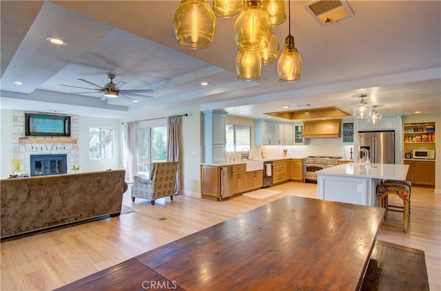 dining area featuring ceiling fan, a tray ceiling, light hardwood / wood-style flooring, a fireplace, and sink