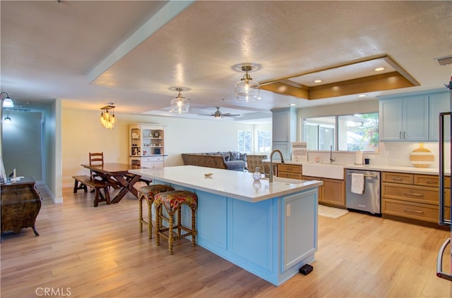 kitchen featuring dishwasher, light hardwood / wood-style flooring, a tray ceiling, a center island with sink, and sink