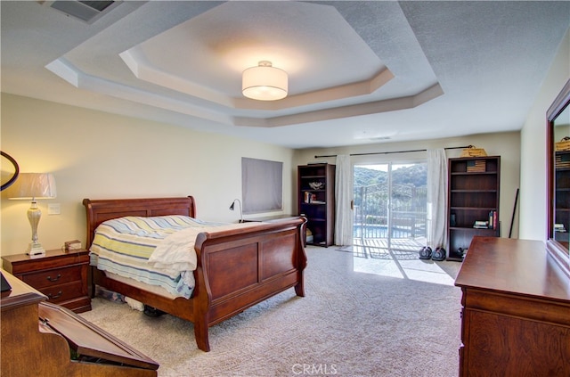 bedroom with access to outside, a tray ceiling, and light colored carpet