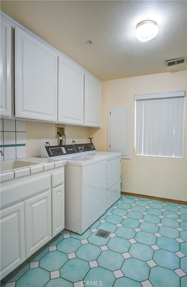 laundry area with cabinets, a textured ceiling, and washing machine and dryer