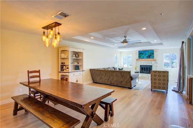 dining space with ceiling fan with notable chandelier, light hardwood / wood-style flooring, a tray ceiling, and a fireplace