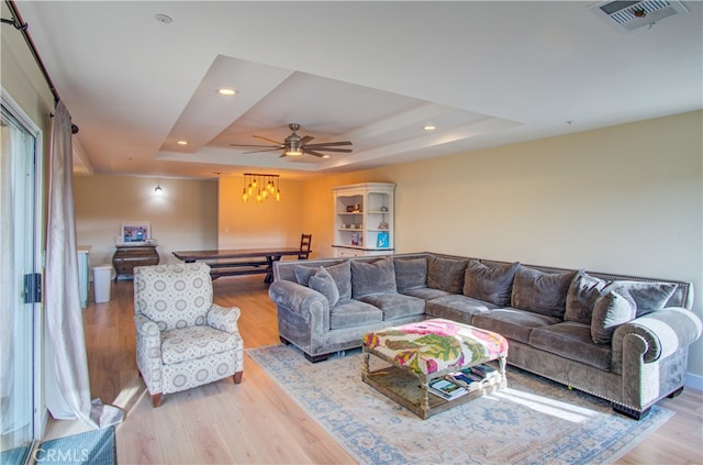 living room featuring light hardwood / wood-style flooring, ceiling fan, and a raised ceiling