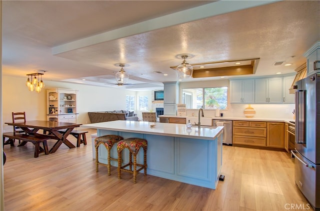 kitchen featuring light wood-type flooring, a textured ceiling, a tray ceiling, stainless steel appliances, and a kitchen island with sink