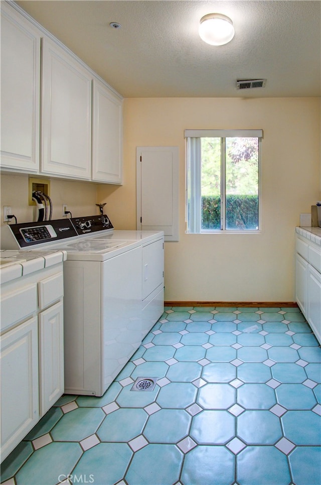 laundry room with independent washer and dryer, a textured ceiling, and cabinets