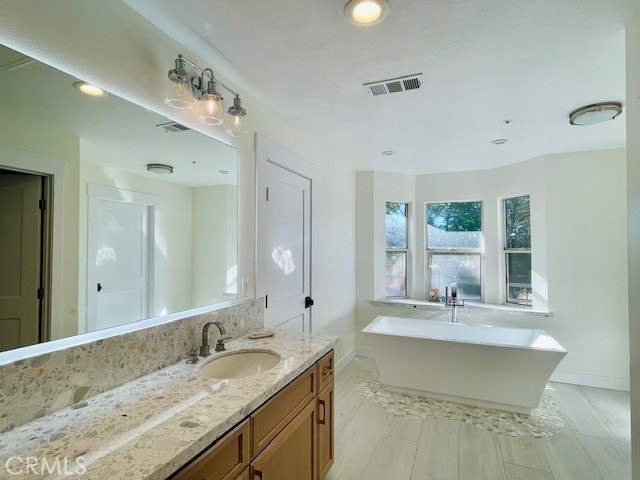 bathroom featuring vanity, a tub to relax in, and wood-type flooring