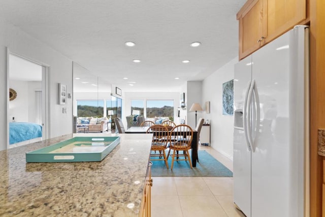 kitchen with white refrigerator with ice dispenser, white cabinets, light tile patterned floors, light brown cabinetry, and light stone counters