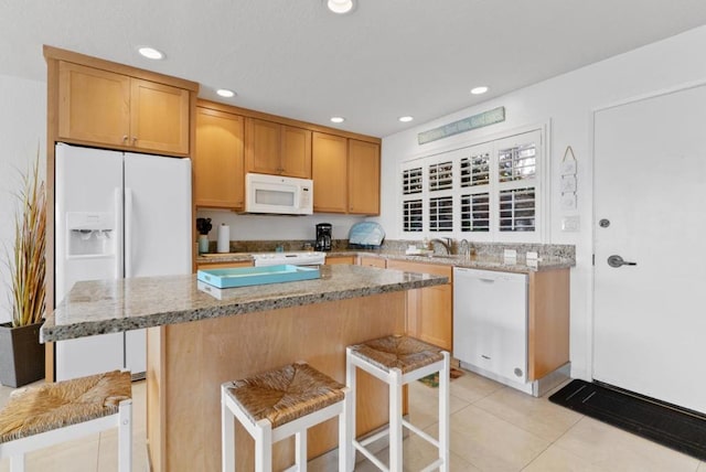 kitchen featuring a kitchen breakfast bar, light stone counters, white appliances, sink, and light tile patterned floors