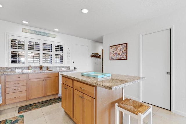 kitchen with a kitchen bar, a kitchen island, light stone countertops, and light tile patterned floors