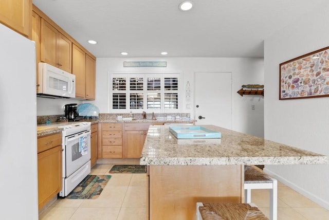 kitchen with light stone counters, white appliances, a center island, a breakfast bar area, and light tile patterned flooring