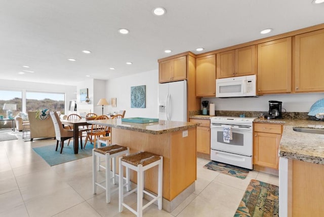 kitchen featuring a kitchen bar, light stone counters, white appliances, light tile patterned floors, and a center island