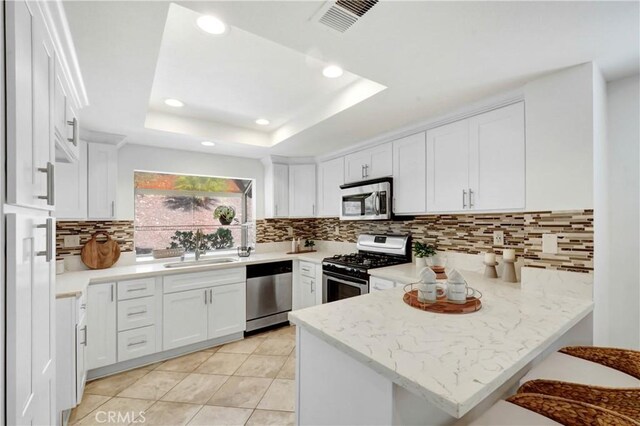 kitchen featuring sink, white cabinetry, appliances with stainless steel finishes, a tray ceiling, and kitchen peninsula