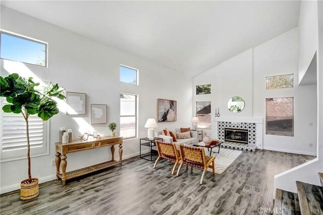 living room featuring a tiled fireplace, a healthy amount of sunlight, high vaulted ceiling, and wood-type flooring