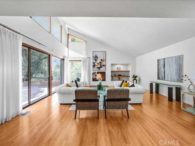 living area featuring light wood-style flooring, visible vents, high vaulted ceiling, and built in shelves
