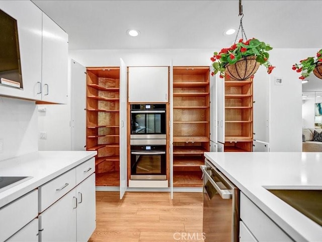 kitchen with appliances with stainless steel finishes, white cabinetry, light countertops, and light wood finished floors