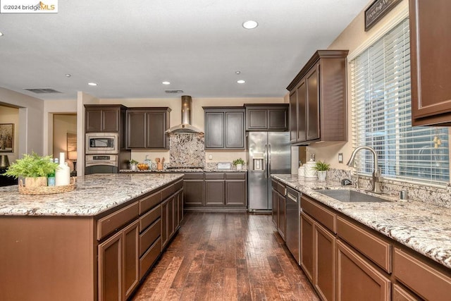 kitchen featuring wall chimney range hood, appliances with stainless steel finishes, sink, dark wood-type flooring, and light stone counters