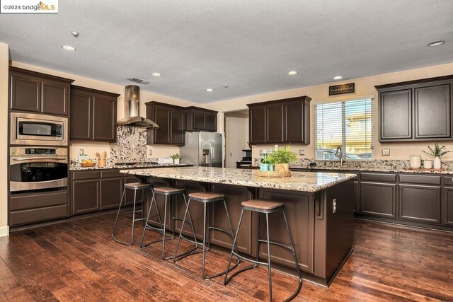 kitchen featuring wall chimney exhaust hood, stainless steel appliances, dark wood-type flooring, and a kitchen island