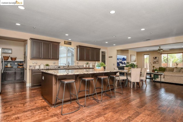 kitchen featuring dark wood-type flooring, a large island, a kitchen bar, dark brown cabinetry, and light stone counters