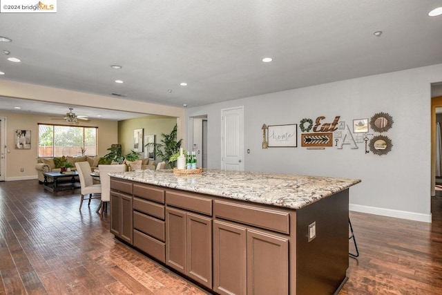 kitchen featuring dark wood-type flooring, a breakfast bar, light stone countertops, a center island, and ceiling fan