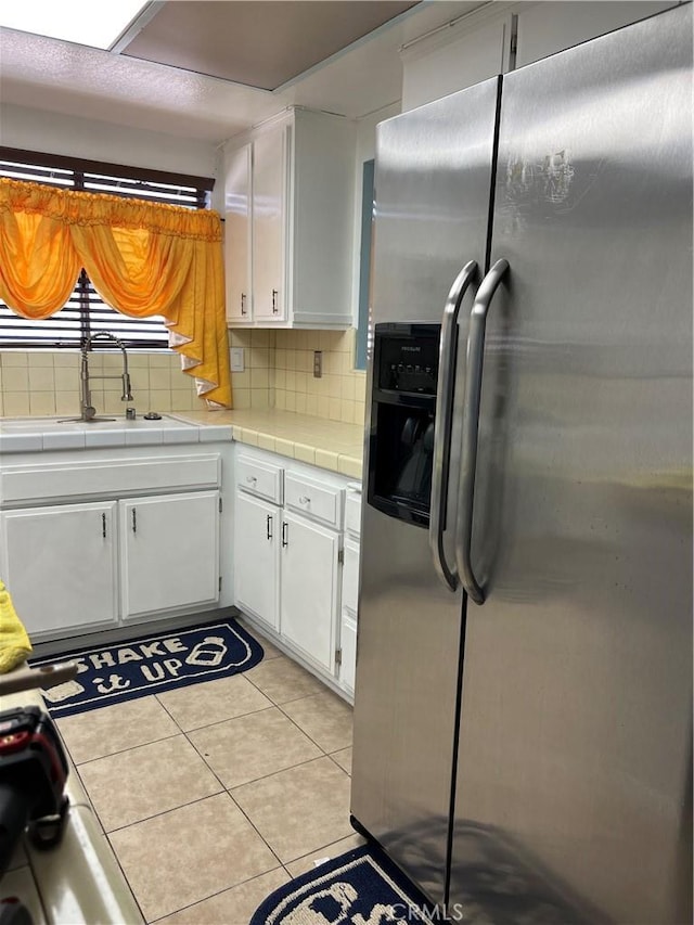 kitchen featuring stainless steel fridge, tasteful backsplash, white cabinetry, and tile counters