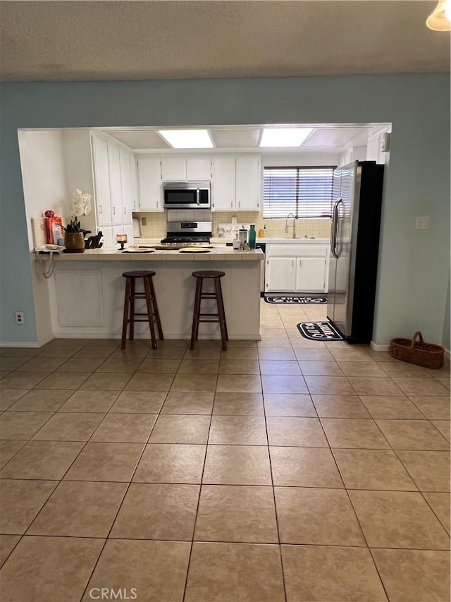 kitchen with a breakfast bar, white cabinets, sink, kitchen peninsula, and stainless steel appliances