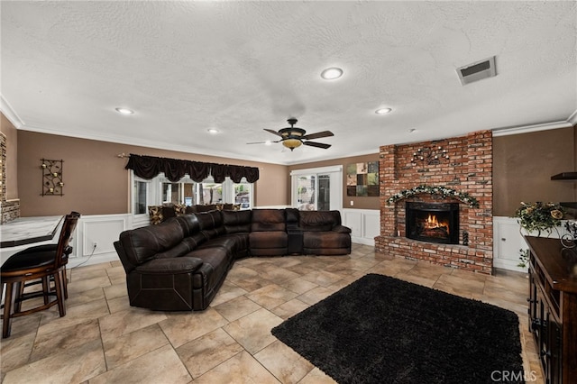 living room featuring a textured ceiling, a fireplace, ceiling fan, and crown molding