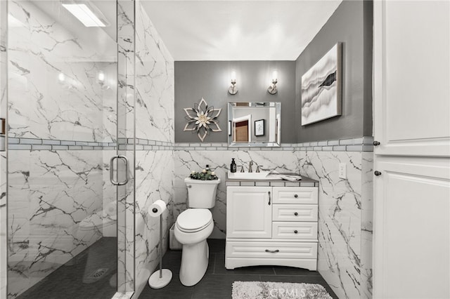 bathroom featuring vanity, a shower with door, tile patterned flooring, toilet, and tile walls