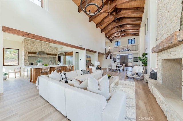 living room featuring high vaulted ceiling, wooden ceiling, light hardwood / wood-style flooring, beamed ceiling, and a stone fireplace