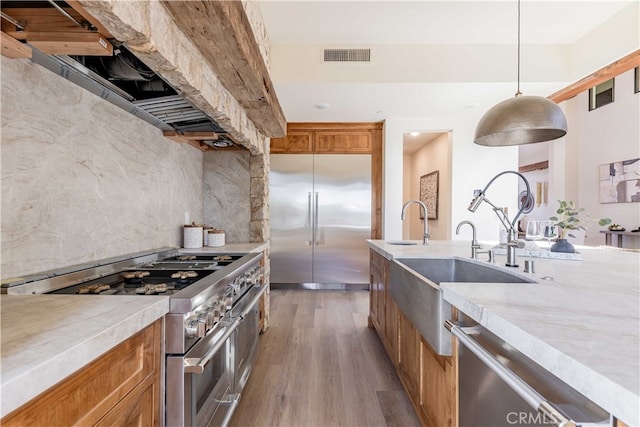 kitchen with premium appliances, wood-type flooring, sink, hanging light fixtures, and decorative backsplash