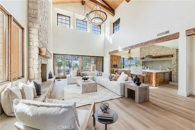 living room with light hardwood / wood-style floors, beamed ceiling, sink, a fireplace, and high vaulted ceiling