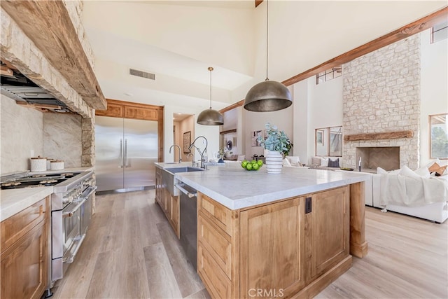 kitchen featuring a towering ceiling, light hardwood / wood-style floors, pendant lighting, high end appliances, and a center island with sink