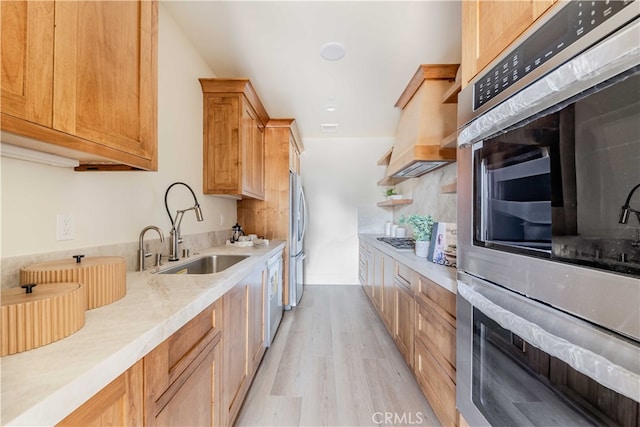 kitchen featuring wall chimney range hood, appliances with stainless steel finishes, sink, light wood-type flooring, and backsplash